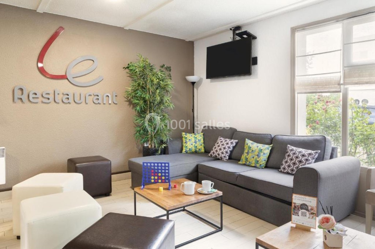 Salon d'attente avec canapé, table basse, jeux de société, et décoration végétale près d'un mur avec logo ’Restaurant’.