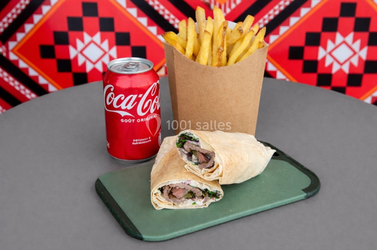 Un wrap garni de viande et légumes, accompagné de frites et d'une canette de soda sur une table grise.