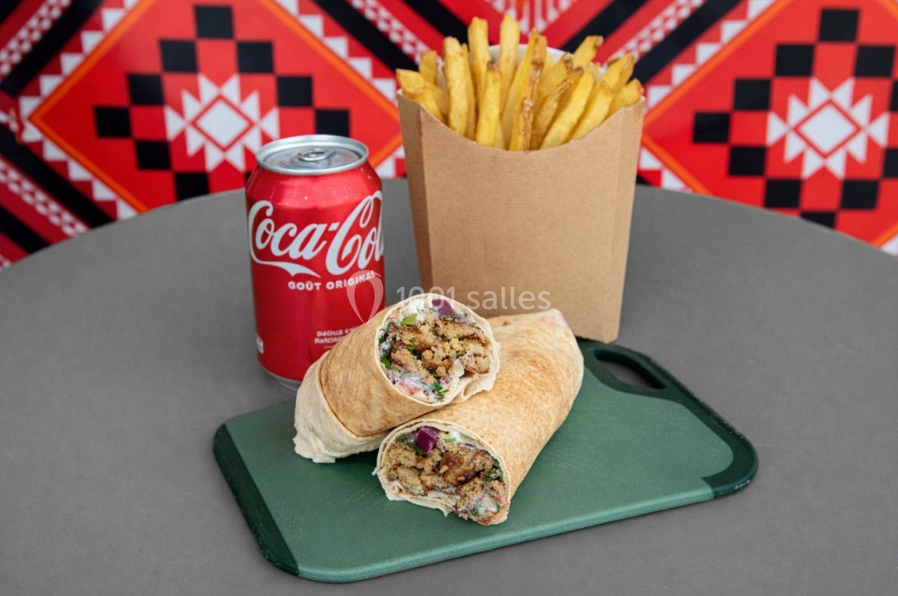 Un wrap garni coupé en deux, accompagné de frites et d'une canette de soda, sur une table grise.