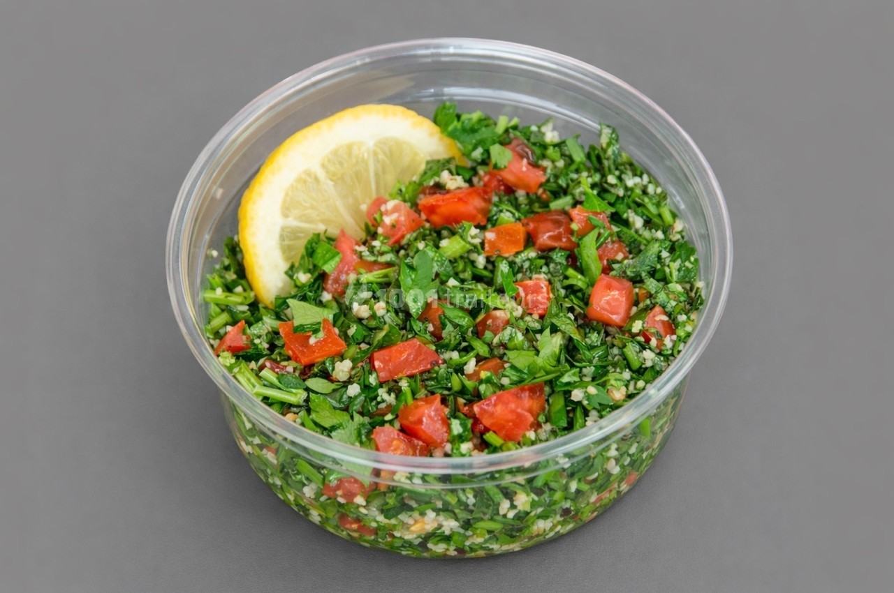 Salade taboulé dans un bol transparent, garnie de persil, tomates, boulgour et une tranche de citron.