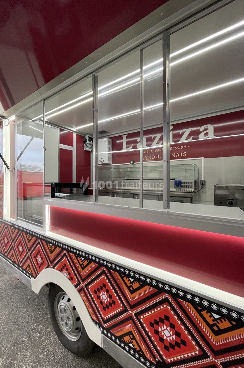 Camion de restauration rouge avec motifs géométriques, vitrine ouverte et intérieur équipé pour la préparation alimentaire.