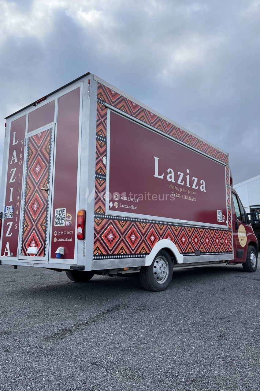 Camion de restauration rapide avec motifs orientaux et logo ’Laziza’, stationné sur un parking sous un ciel nuageux.