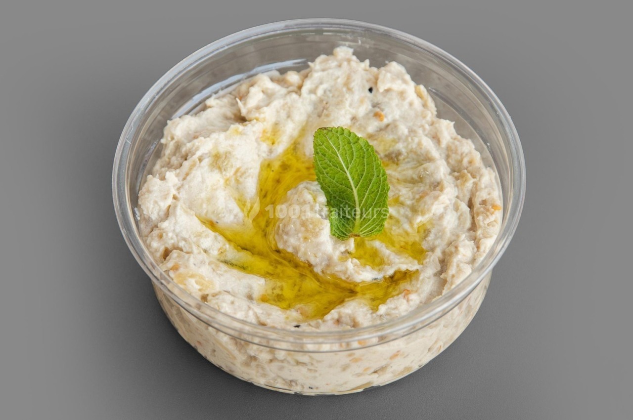 Bol transparent contenant du houmous garni d'une feuille de menthe et d'un filet d'huile d'olive.