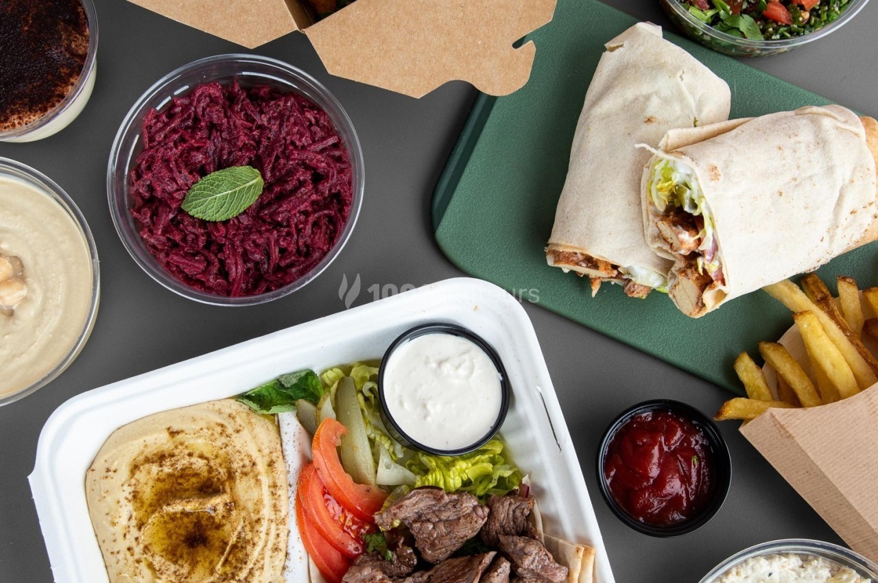 Assortiment de plats méditerranéens avec viandes grillées, wraps, houmous, salades, frites et sauces.