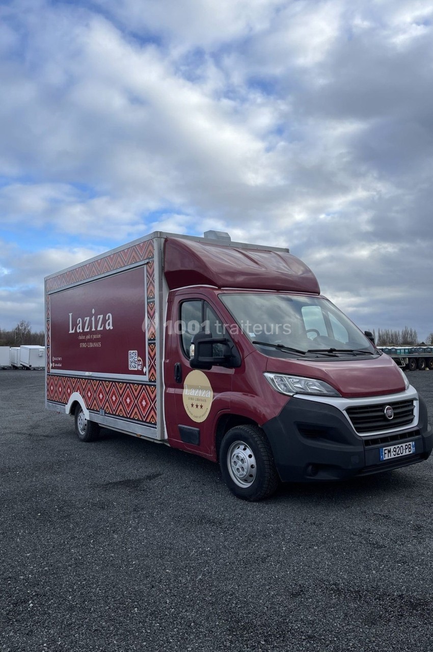 Camion rouge Laziza stationné sur un parking, avec un ciel nuageux en arrière-plan.