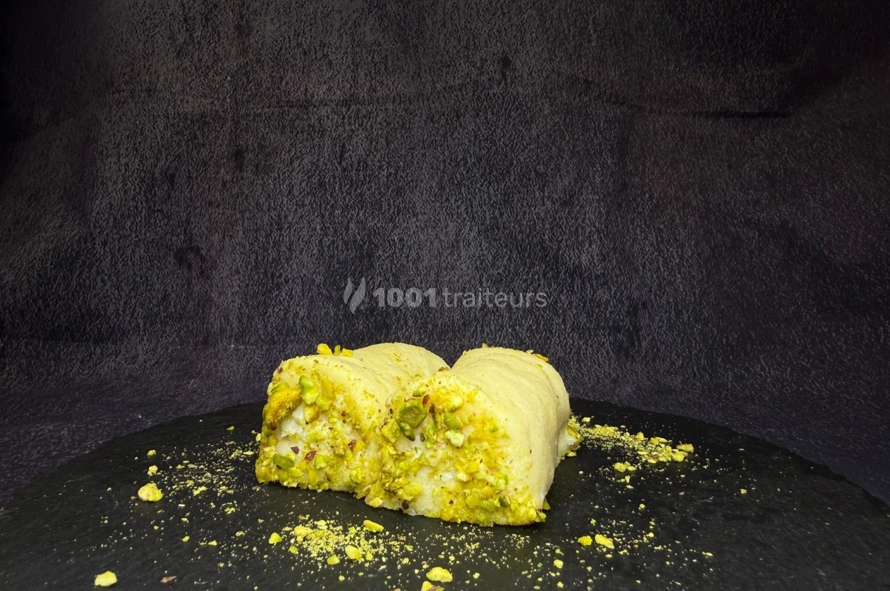 Deux morceaux de pâtisserie à base de pistaches, posés sur une surface noire avec un fond sombre.