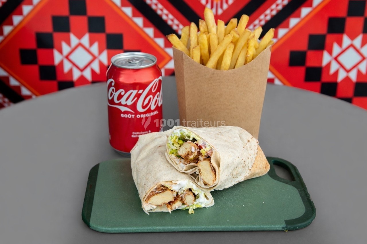 Un wrap garni, des frites dans un contenant en carton et une canette de soda sur une table grise.