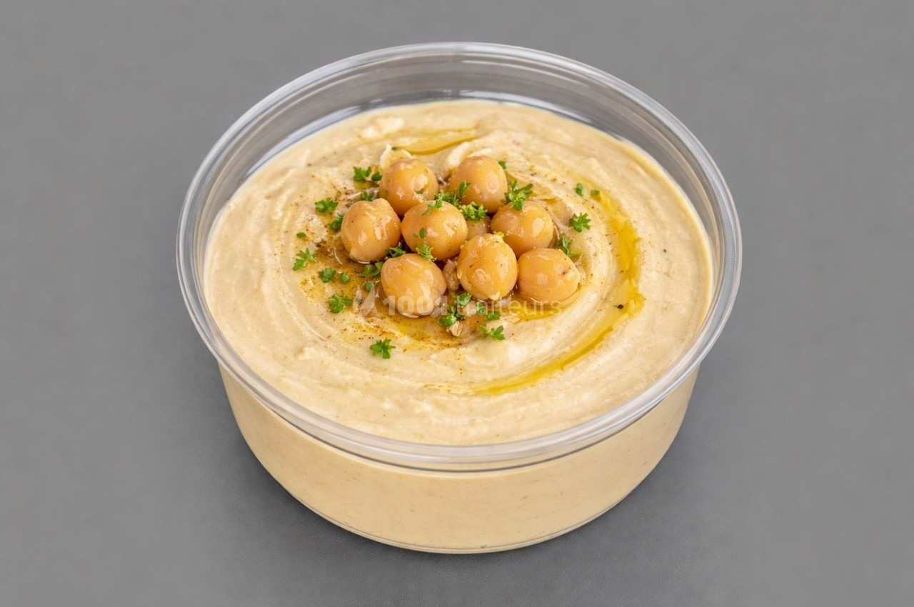 Bol de houmous garni de pois chiches entiers, persil haché et filet d'huile d'olive, sur fond gris.