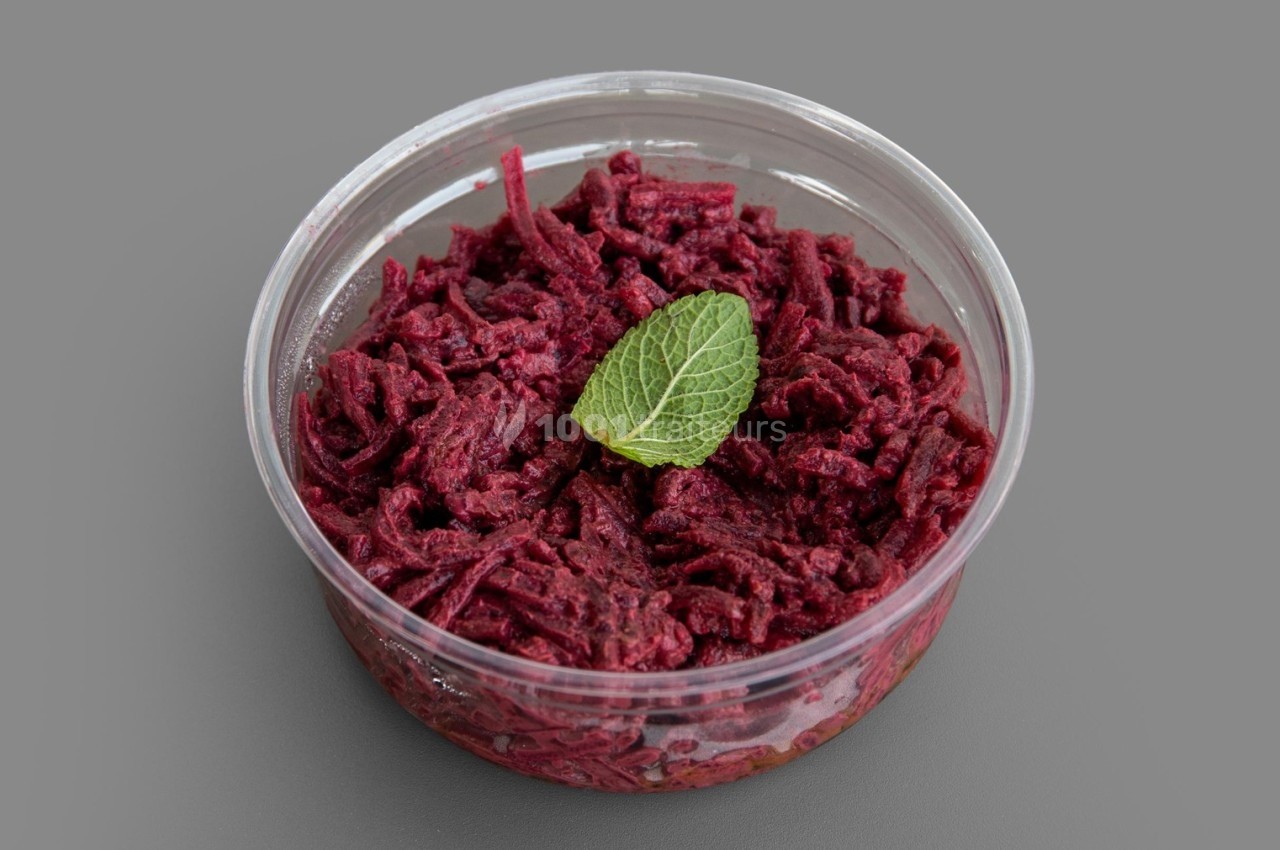 Salade de betteraves râpées dans un récipient transparent, garnie d'une feuille de menthe sur un fond gris.