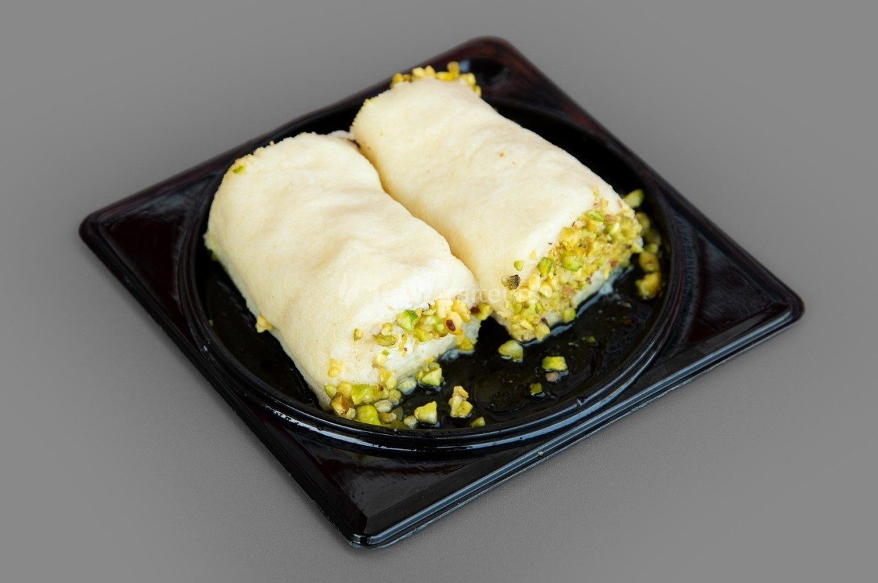 Deux pâtisseries roulées garnies de pistaches hachées, présentées sur une assiette noire.