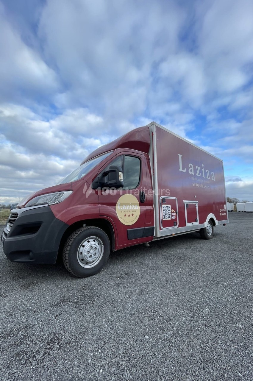 Camion rouge Laziza stationné sur un sol gravillonné, sous un ciel partiellement nuageux.