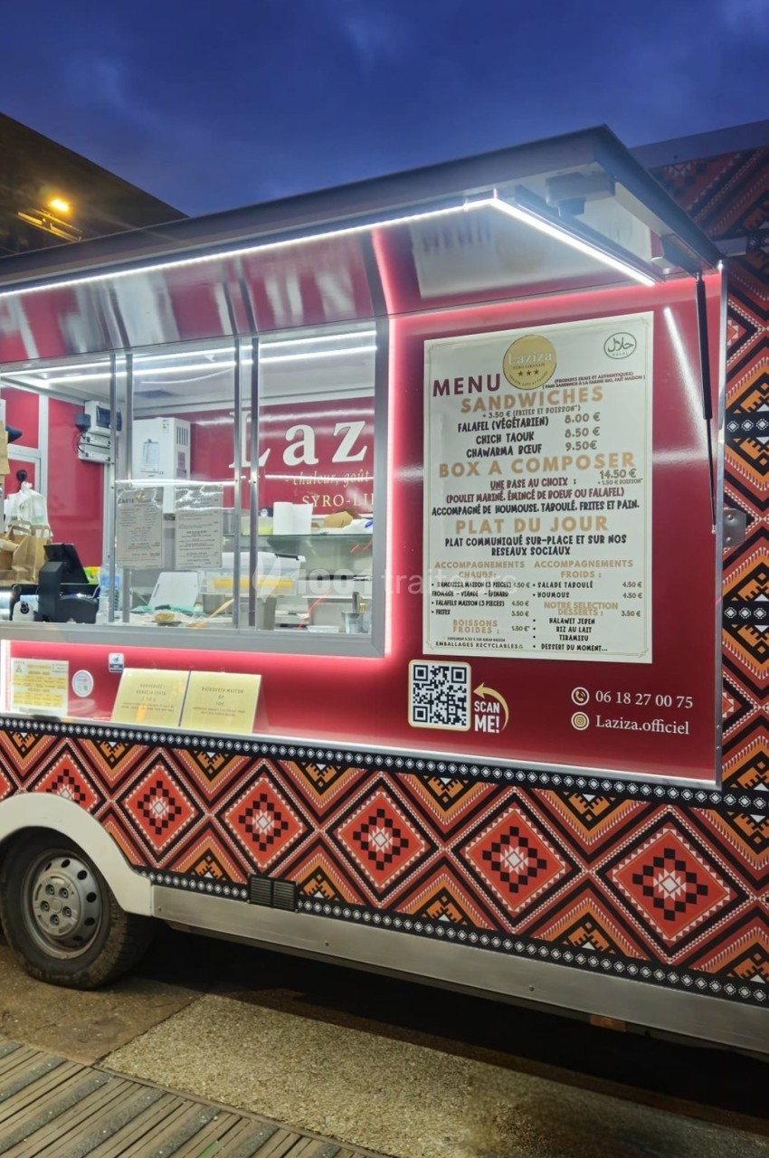 Camion de street food avec menu affiché sur le côté, décoré de motifs colorés et éclairé en soirée.