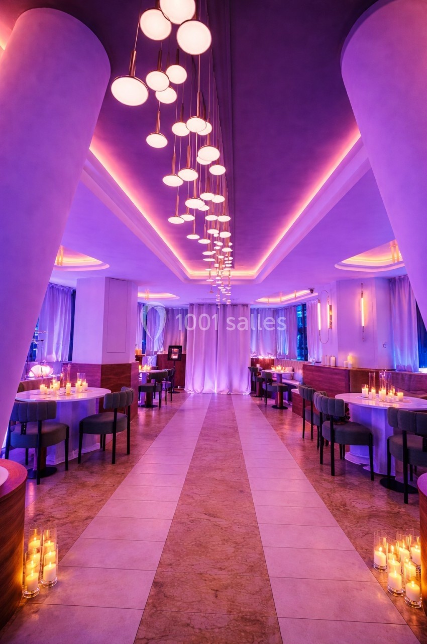 Salle de restaurant élégante avec éclairage violet, tables dressées et bougies disposées au sol.