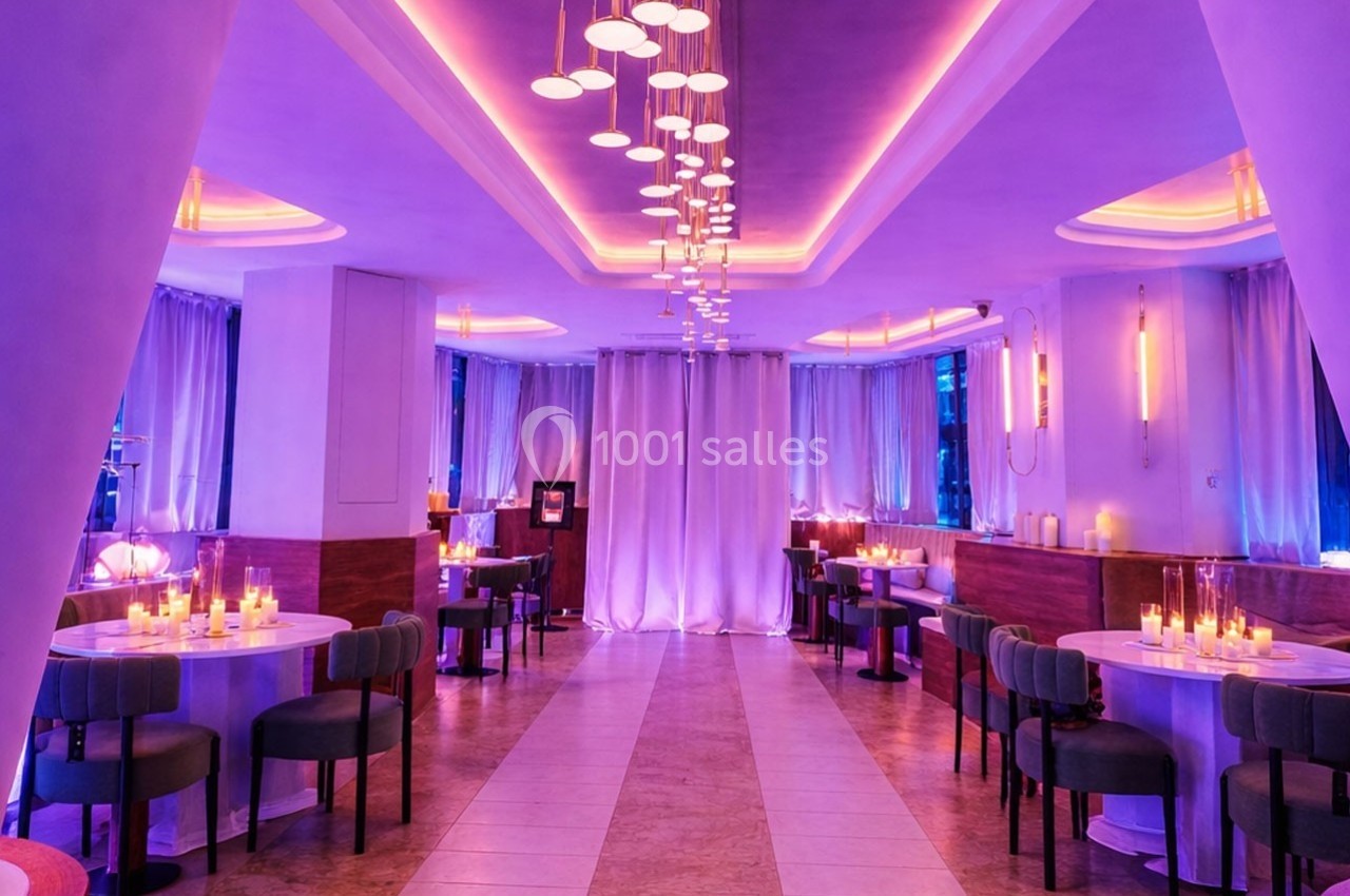 Salle de restaurant moderne avec éclairage violet, tables dressées et bougies créant une ambiance chaleureuse.