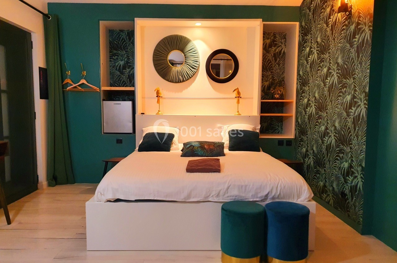 Chambre décorée avec un lit double, murs verts, miroirs ronds, lampes dorées et tabourets en velours.