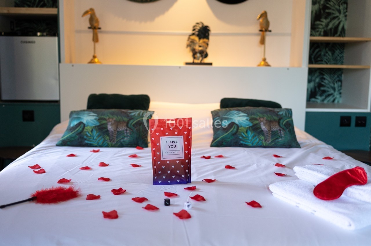 Lit décoré avec des pétales de rose, une boîte cadeau, une plume rouge et des serviettes pliées dans une chambre élégante.