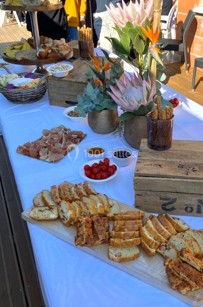 Buffet en extérieur avec planches de charcuterie, pains, tomates cerises, sauces et décorations florales.