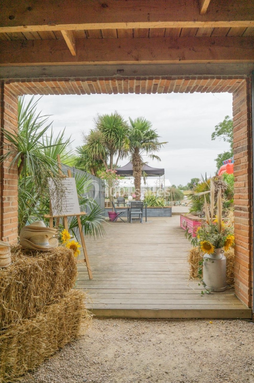 Entrée d'une terrasse en bois avec des palmiers, des bottes de paille décorées et des fleurs jaunes.