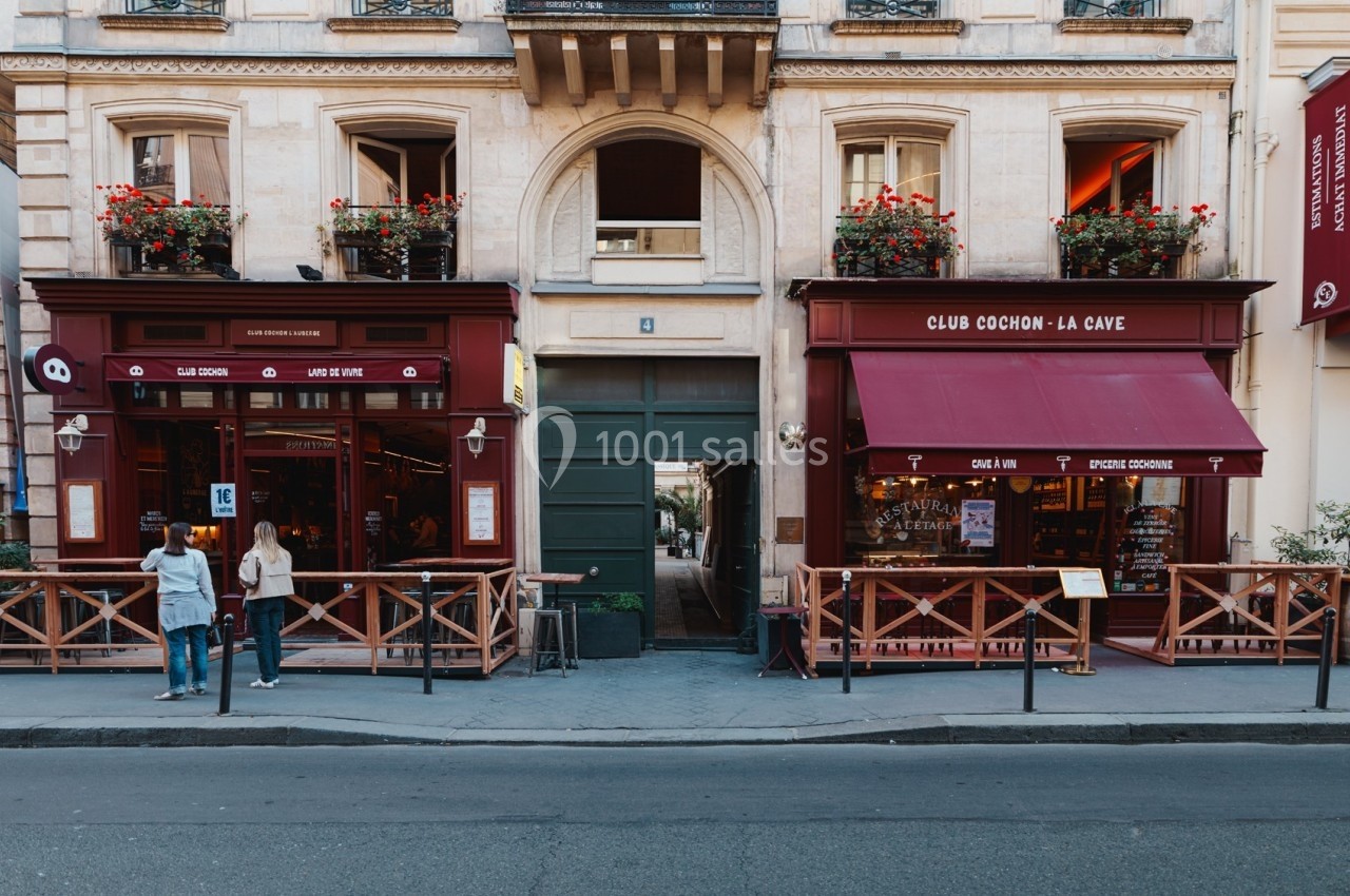 Façade de deux restaurants avec terrasses en bois, séparés par une porte cochère, sur une rue calme.