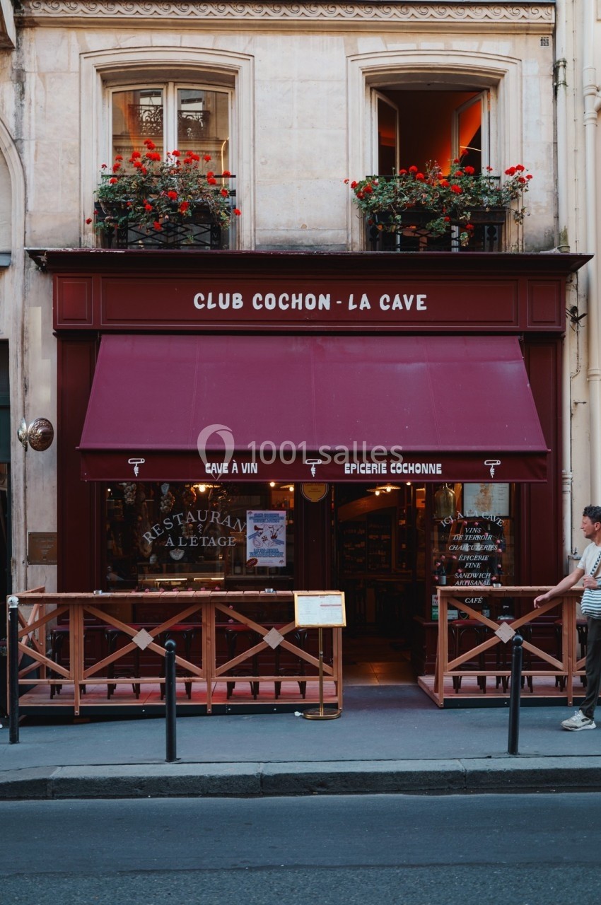 Façade d'une boutique avec auvent rouge, enseigne ’Club Cochon - La Cave’ et fleurs aux fenêtres.
