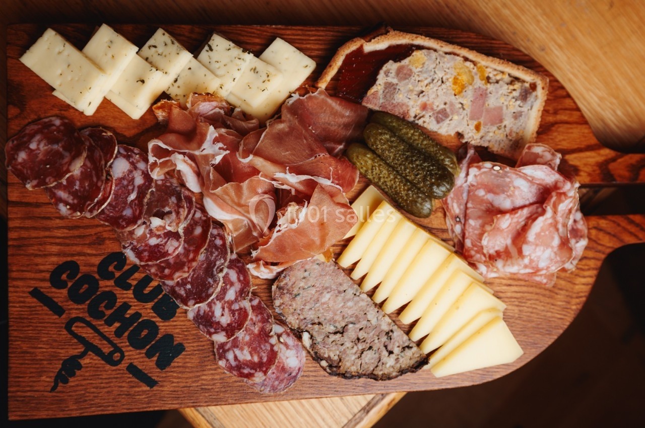 Plateau de charcuterie et fromages avec pâté, cornichons et terrine, présenté sur une planche en bois.