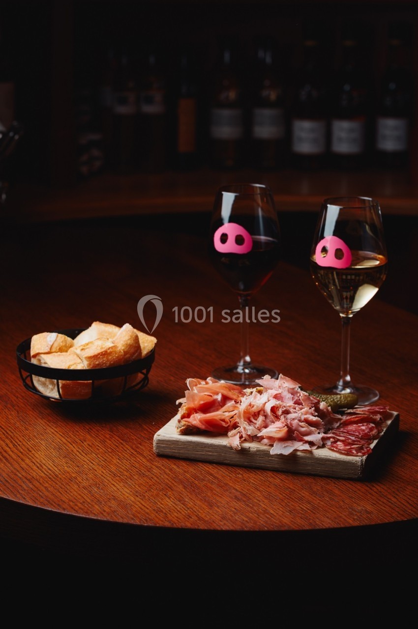 Planche de charcuterie avec deux verres de vin rouge et blanc sur une table en bois, accompagnée d'un panier de pain.