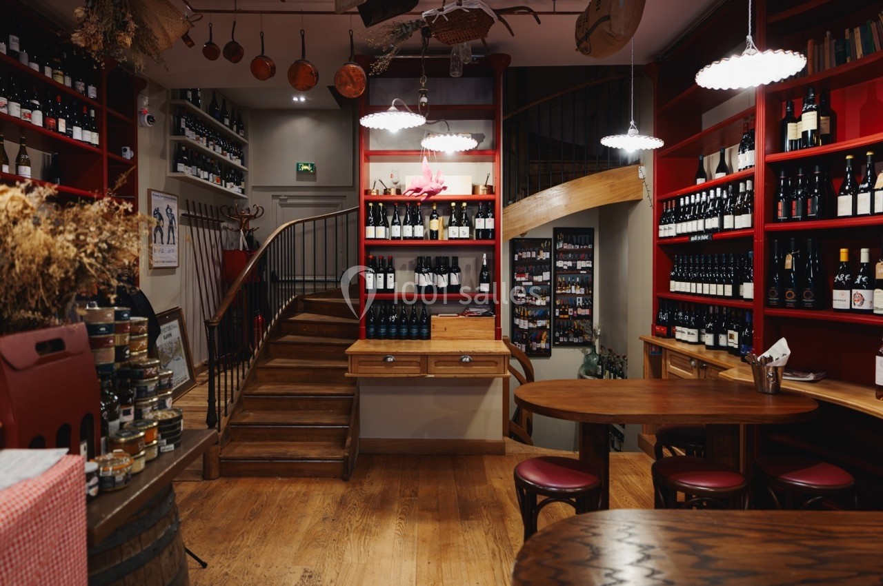 Intérieur d'une cave à vin avec étagères remplies de bouteilles, escalier en bois et tables pour dégustation.