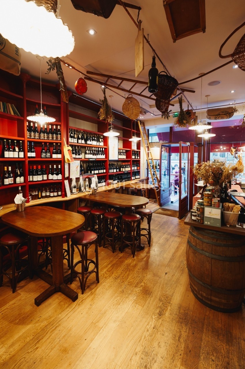Intérieur d'une cave à vin avec étagères remplies de bouteilles, tables en bois et lumière chaleureuse.