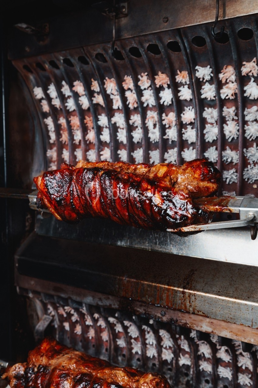 Viande rôtie sur une broche tournante dans un four, avec une cuisson dorée et caramélisée.