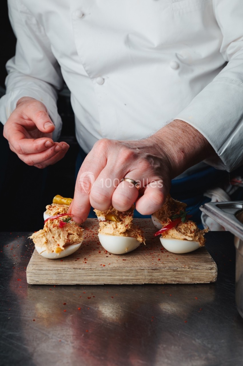 Un chef garnit des œufs farcis avec des ingrédients colorés sur une planche en bois.