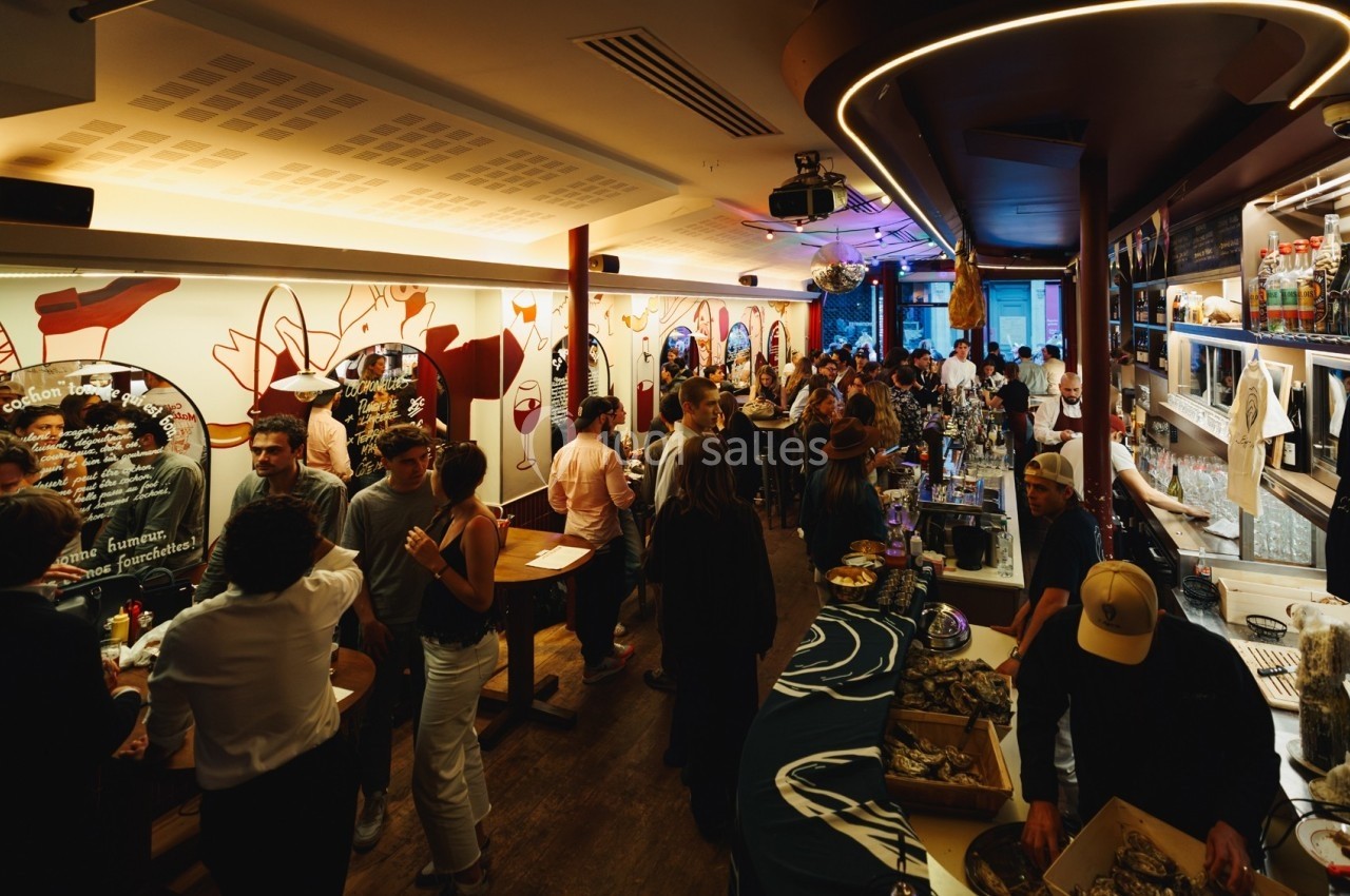 Salle animée avec des personnes discutant et dégustant des huîtres dans un bar à la décoration colorée et moderne.