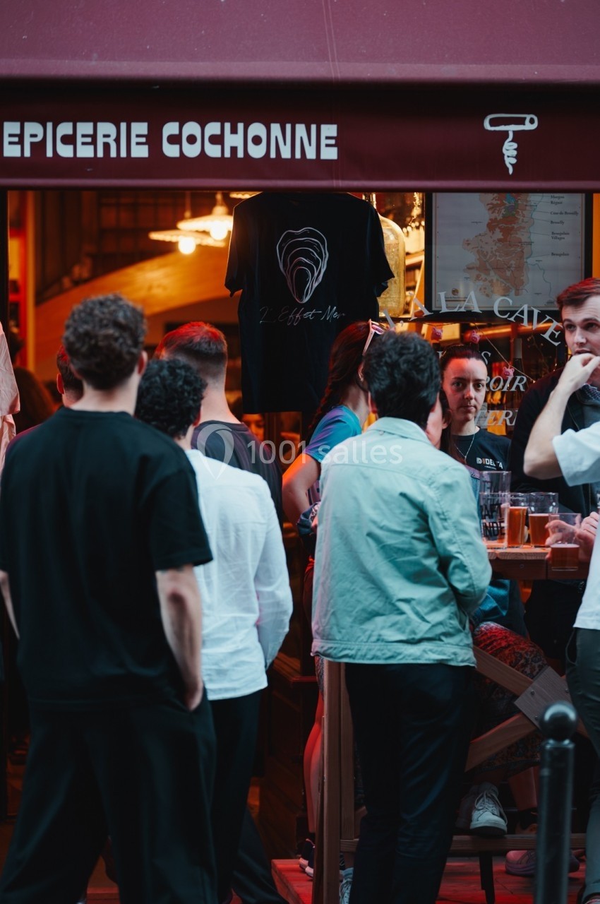 Groupe de personnes discutant et buvant devant une épicerie sous un auvent rouge.