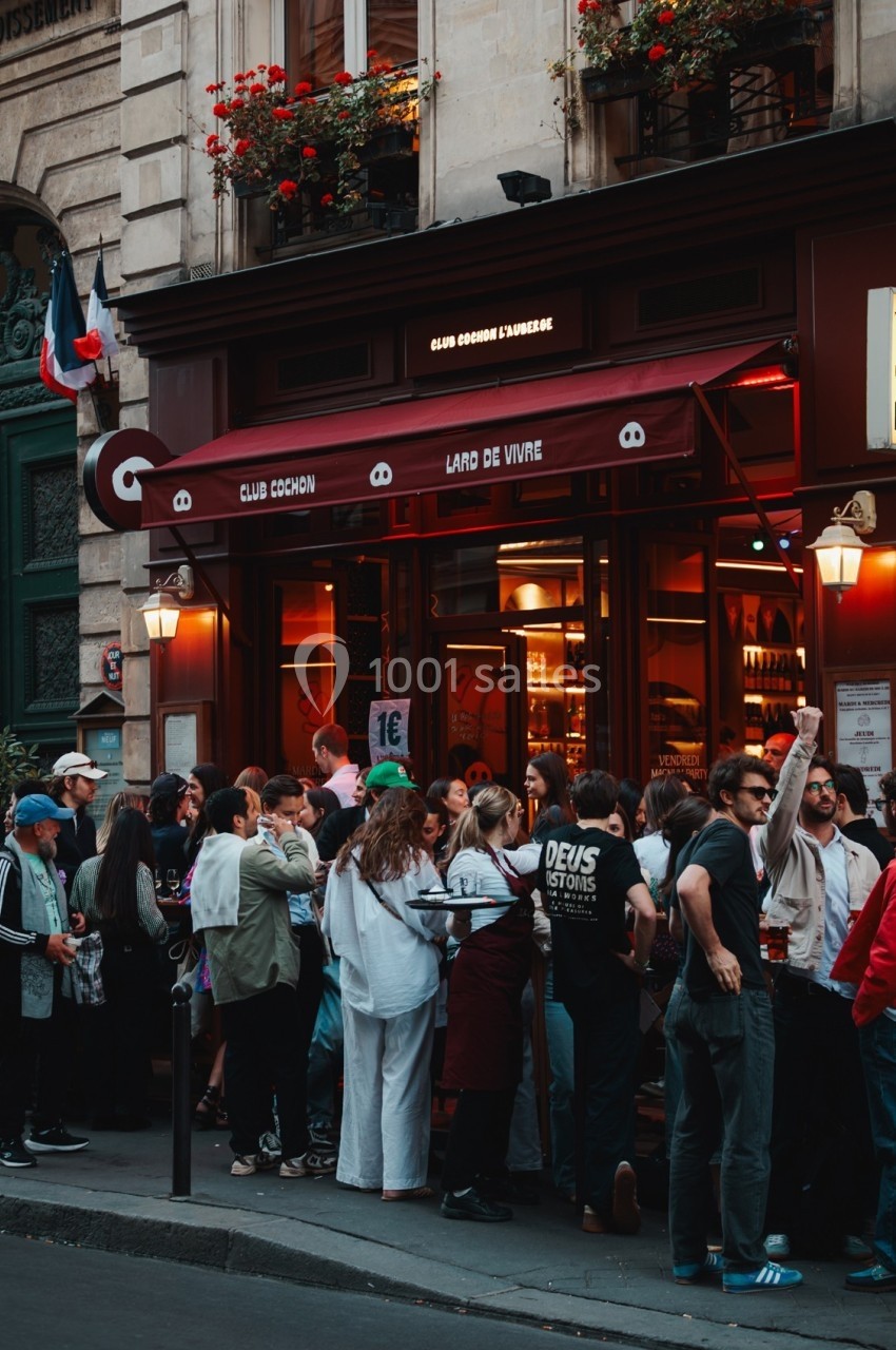 Foule rassemblée devant un bar parisien avec une façade rouge et des enseignes lumineuses.