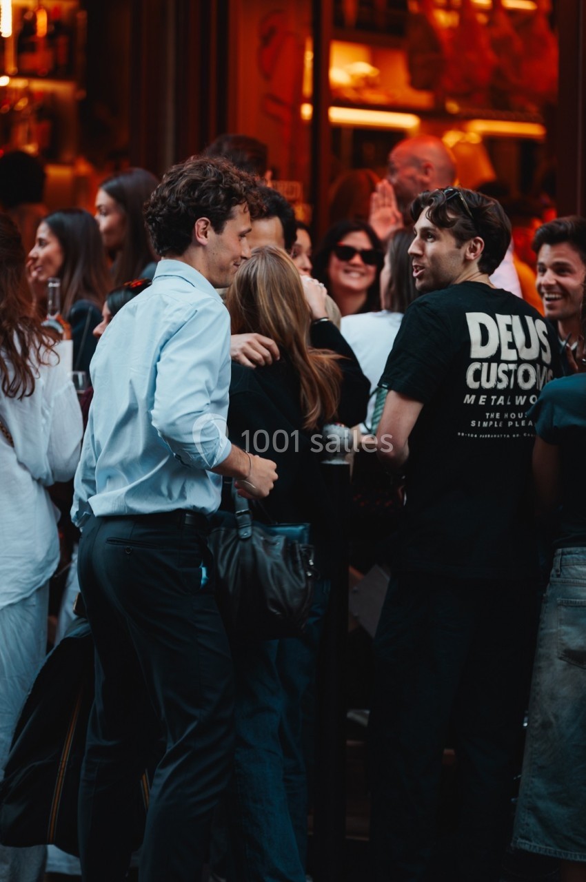 Groupe de personnes discutant et souriant devant l'entrée animée d'un bar ou restaurant en soirée.