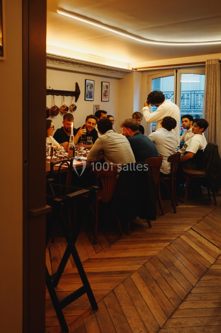 Un groupe de personnes dîne autour d'une grande table dans une pièce chaleureuse avec parquet et éclairage tamisé.