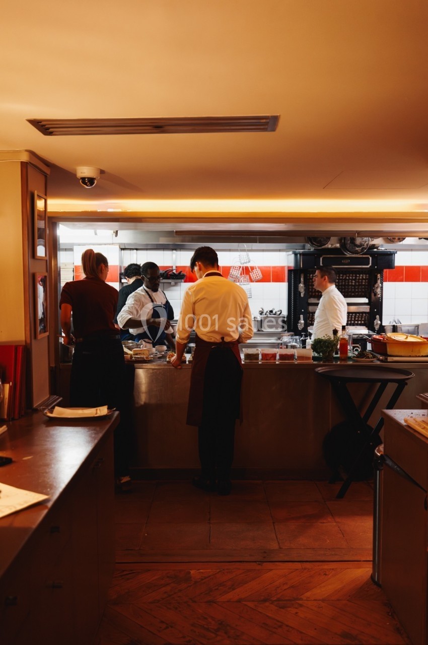 Des chefs et cuisiniers préparent des plats dans une cuisine professionnelle bien éclairée.