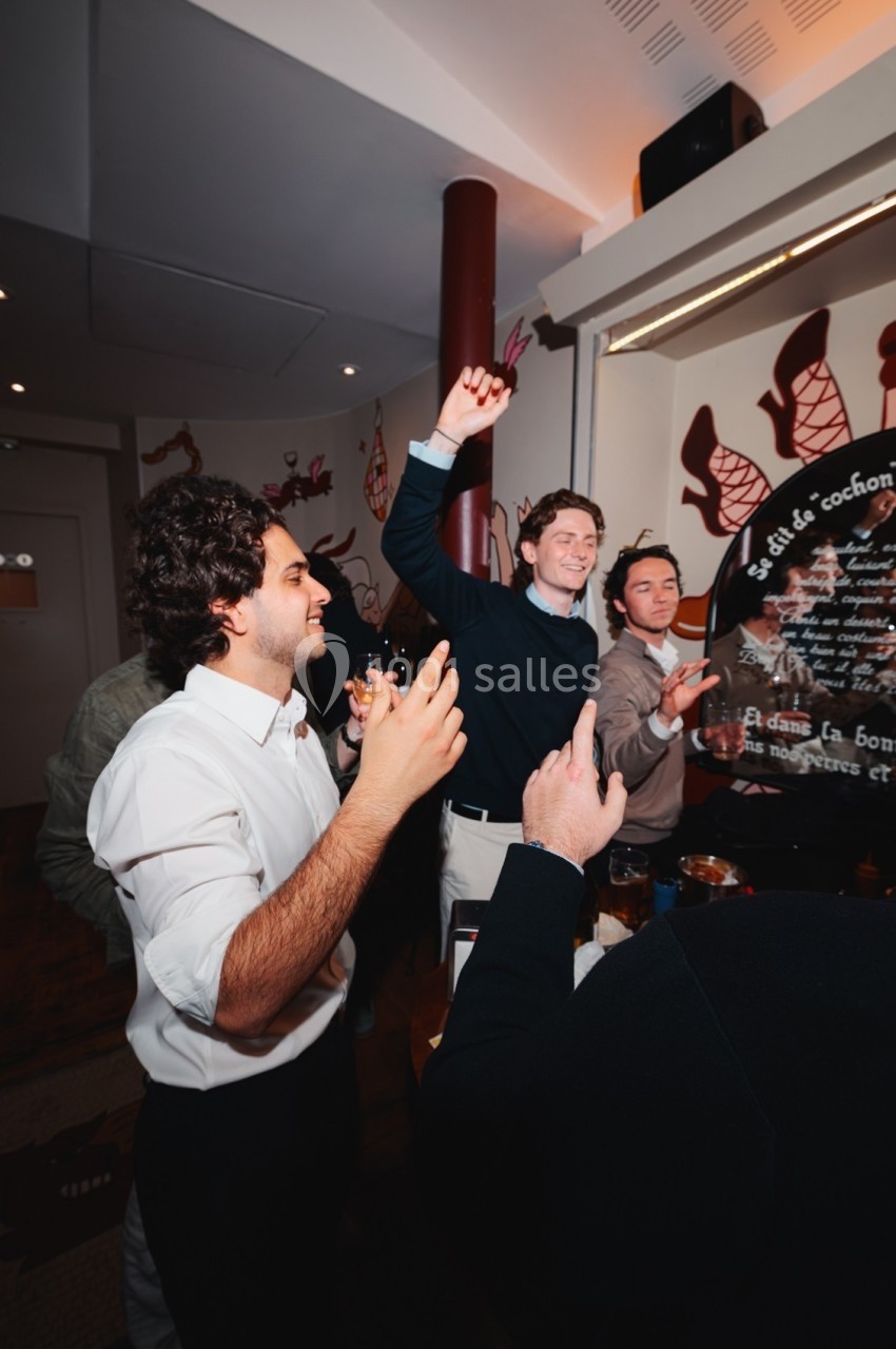 Des personnes souriantes discutent et lèvent les bras dans un intérieur décoré, ambiance conviviale.