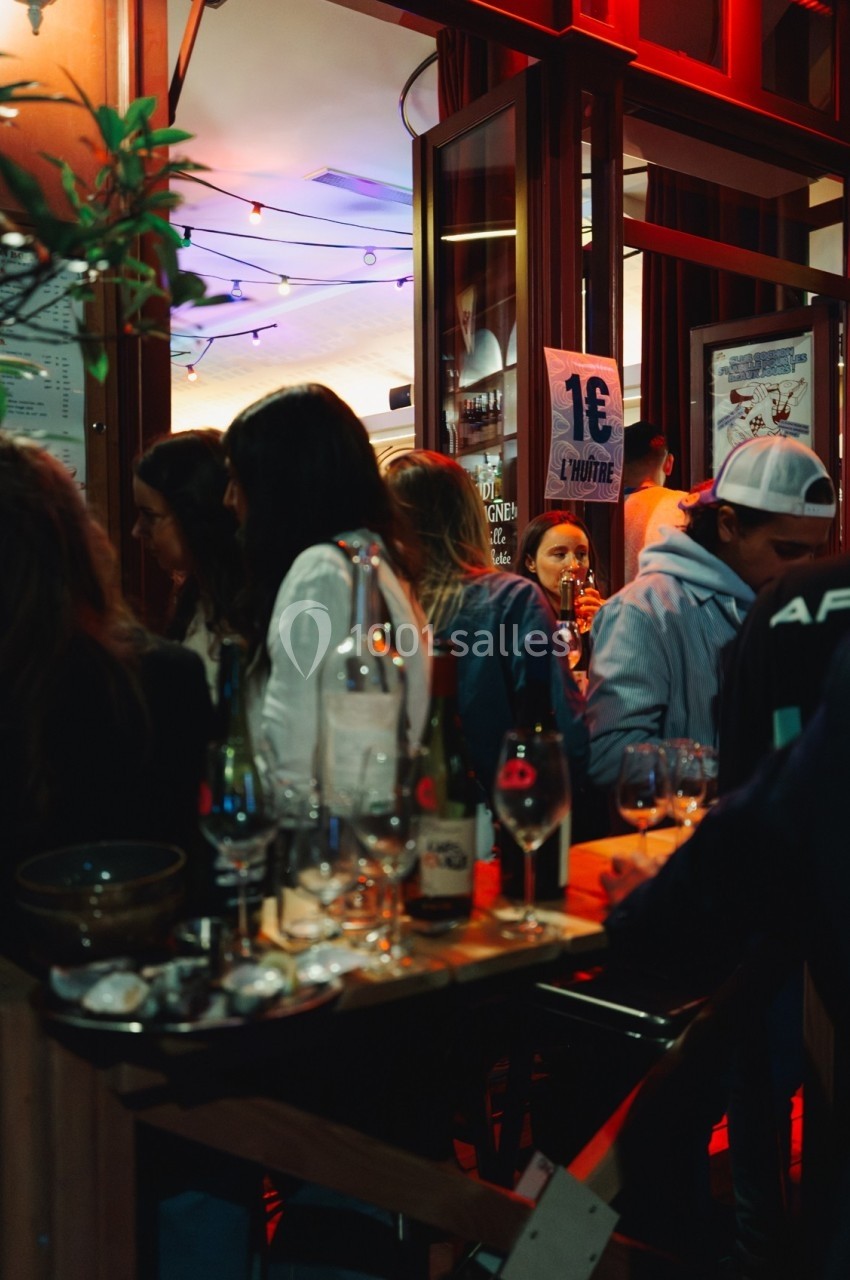 Groupe de personnes discutant et partageant des boissons dans un bar animé éclairé par des lumières chaudes.