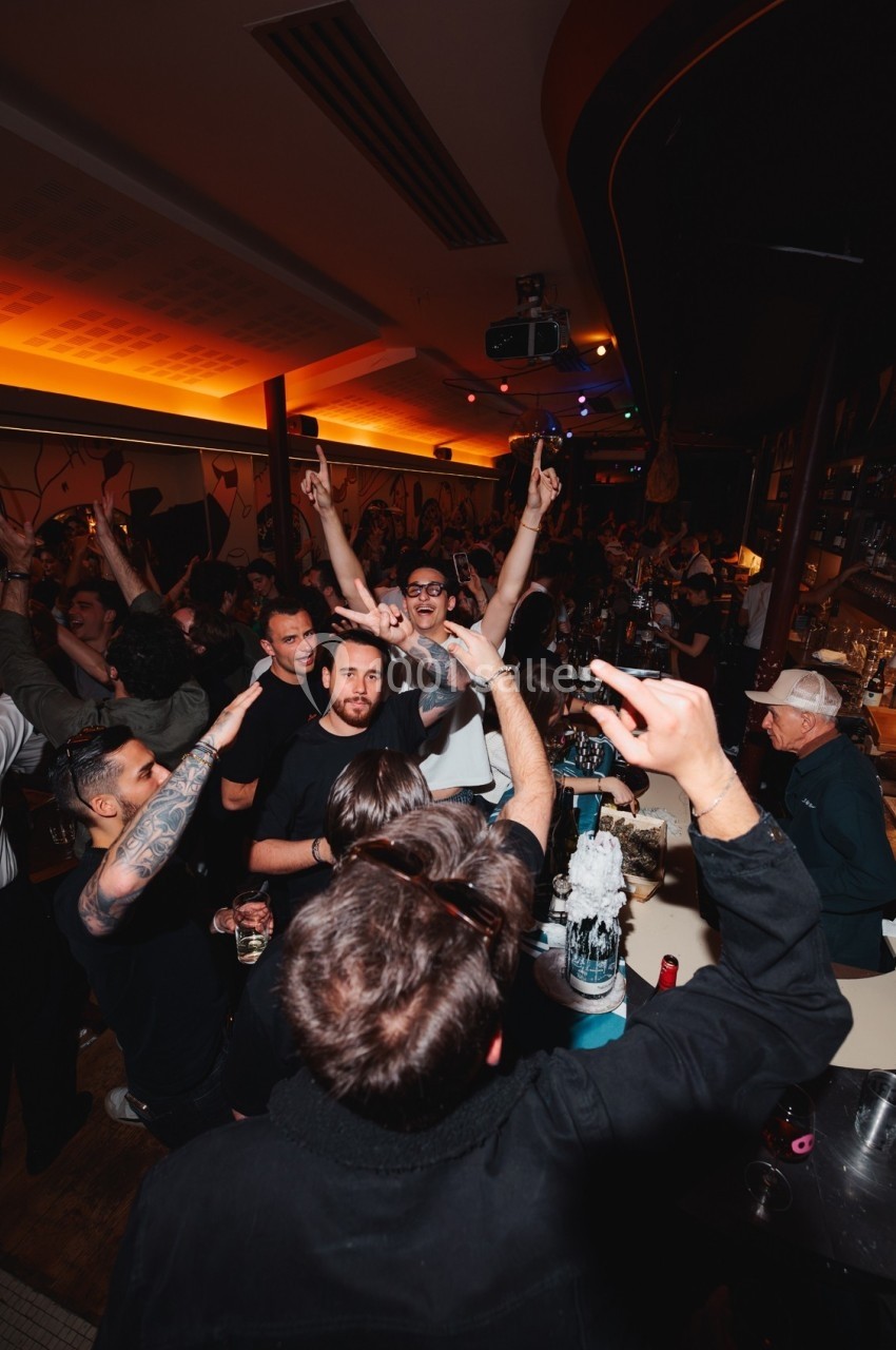 Groupe de personnes célébrant dans un bar animé, avec des bras levés et une ambiance festive.