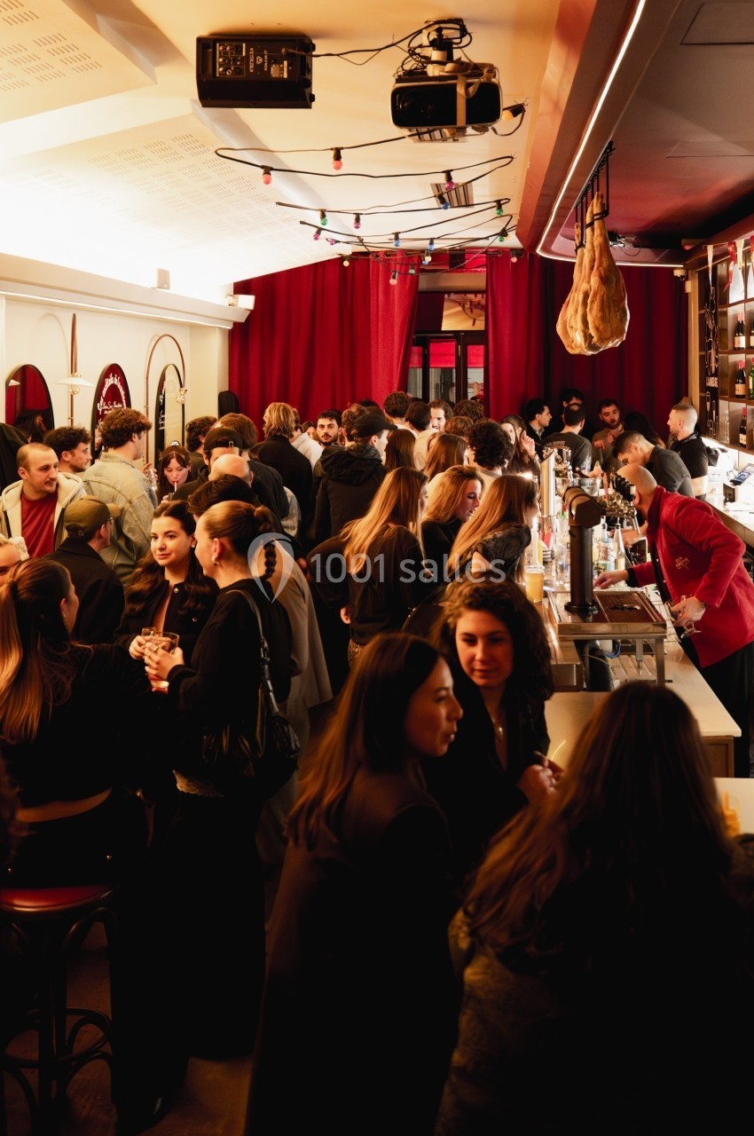 Groupe de personnes discutant et partageant des boissons dans un bar animé avec un éclairage chaleureux.
