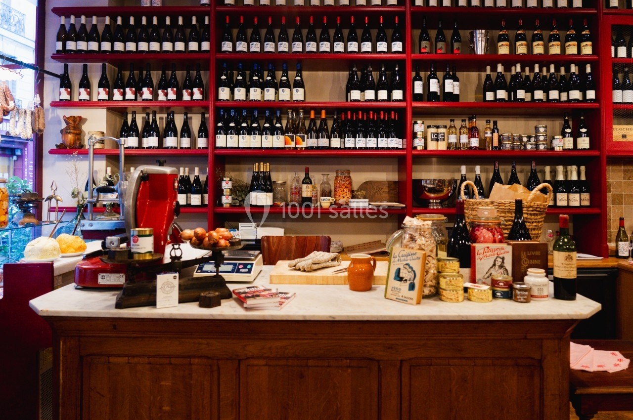 Comptoir en bois dans une épicerie avec étagères remplies de bouteilles de vin et produits artisanaux.