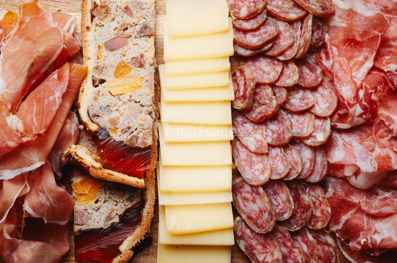 Plateau composé de jambon cru, pâté en croûte, tranches de fromage et saucisson disposés sur une planche en bois.