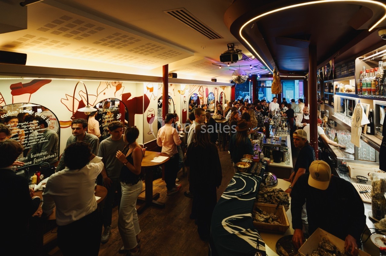 Salle animée d'un bar avec des clients discutant, des décorations murales colorées et un comptoir à huîtres.