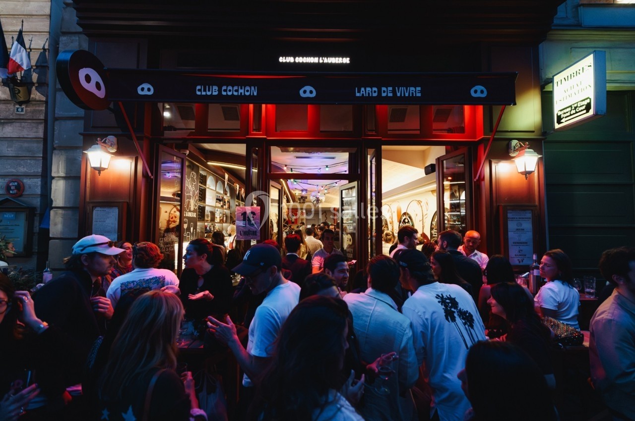 Façade d'un bar animé en soirée, avec une foule rassemblée devant et à l'intérieur sous un éclairage chaleureux.