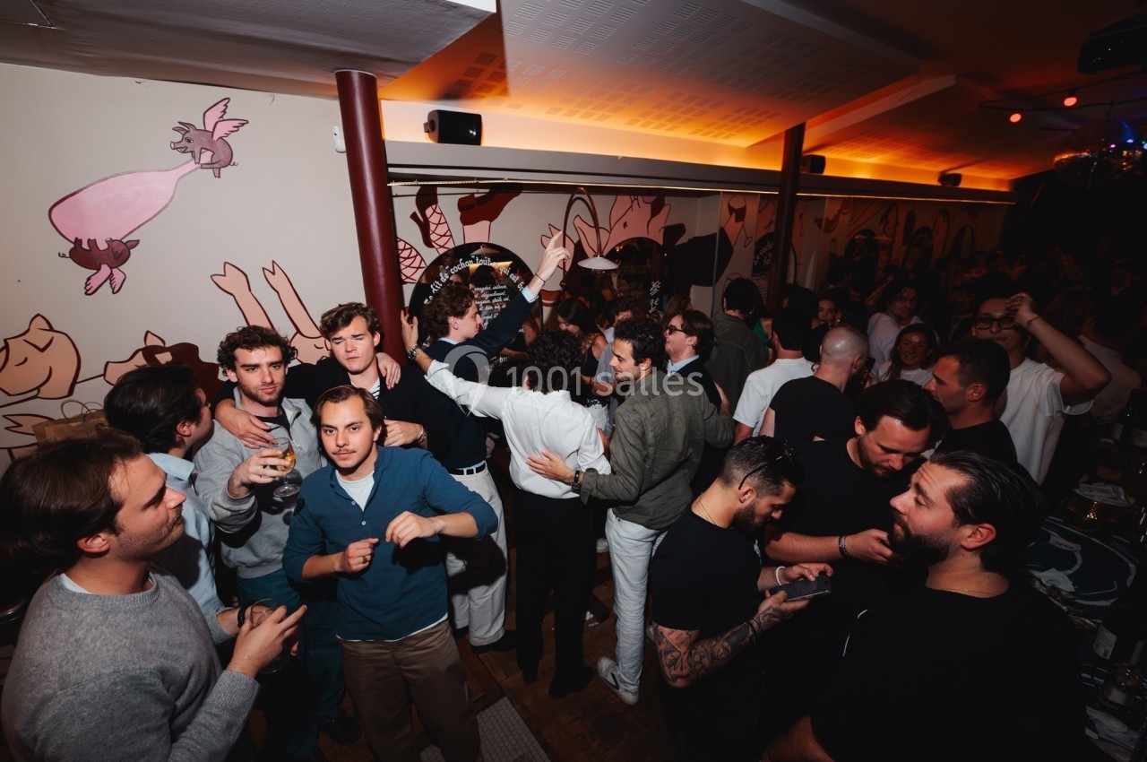 Groupe de personnes discutant et socialisant dans un bar animé avec des fresques murales en arrière-plan.