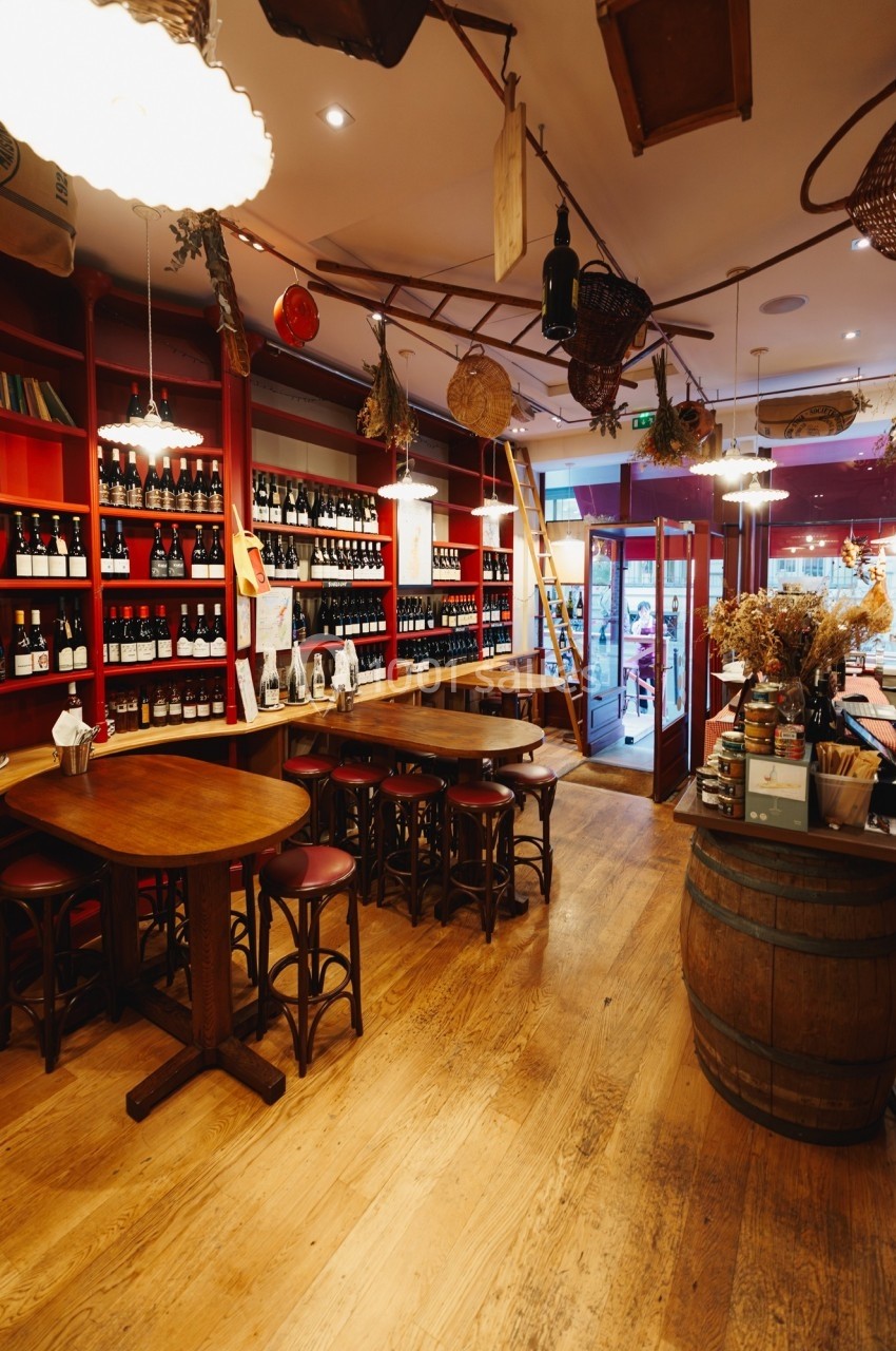 Intérieur d'une cave à vin avec étagères remplies de bouteilles, tables en bois et lumière chaleureuse.