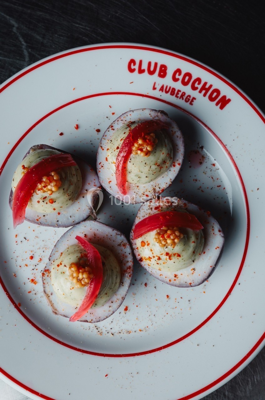 Quatre œufs mimosa garnis de crème, moutarde en grains et pickles, présentés sur une assiette blanche.