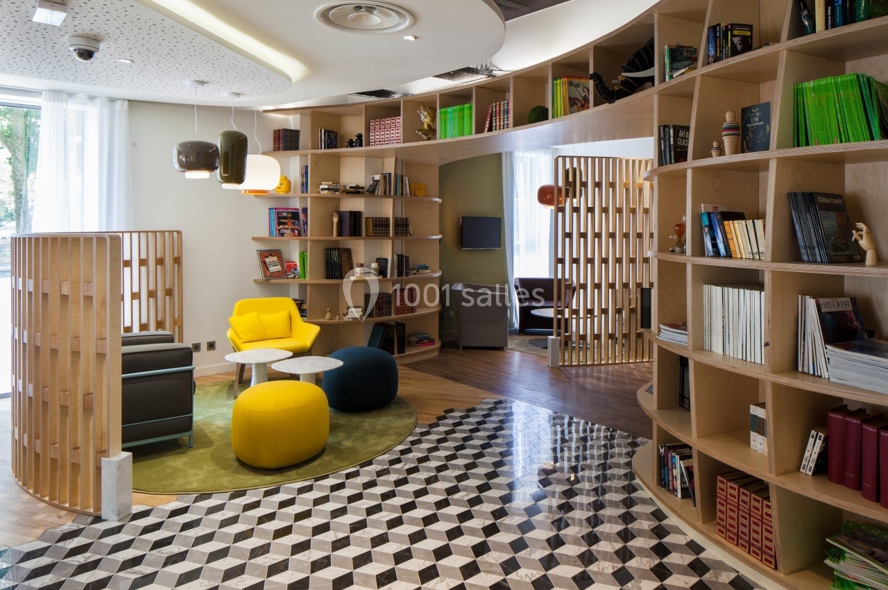 Espace de lecture moderne avec étagères courbes, fauteuils colorés et sol à motifs géométriques.