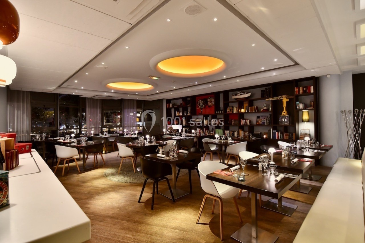 Salle de restaurant moderne avec tables dressées, éclairage chaleureux et étagères décoratives en arrière-plan.