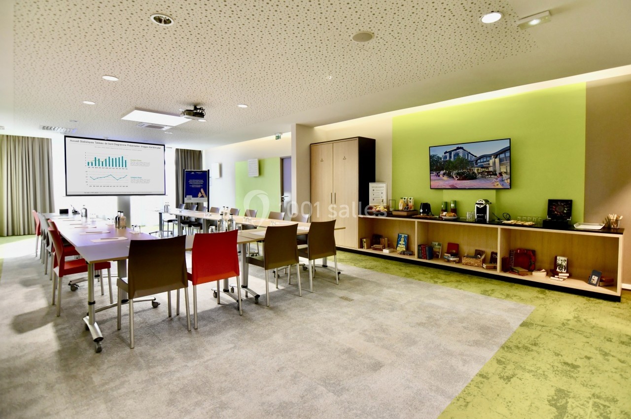 Salle de réunion moderne avec tables, chaises colorées, écran de présentation et étagères décorées.